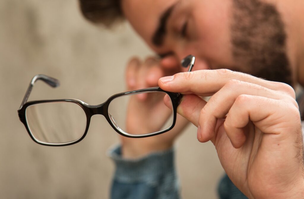 A man holding his glasses for a close-up view as he is blurred in the background rubbing his eye's in discomfort due to a wrong prescription