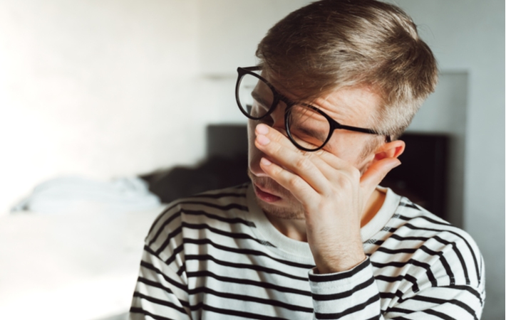 A man lifting his glasses slightly to rub his eye's due to eyestrain from wearing the wrong prescription