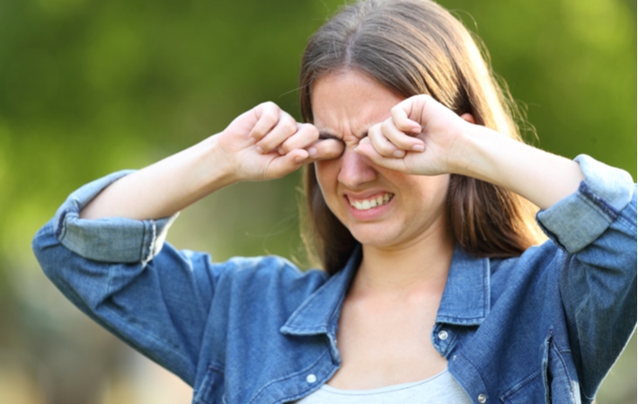 A woman outside rubbing her eyes with a look of pain from summer time allergies