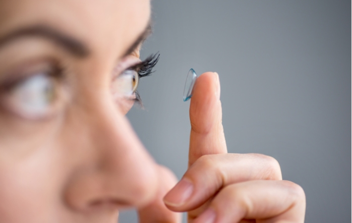 A close up of a woman putting a single use contact onto her left eye