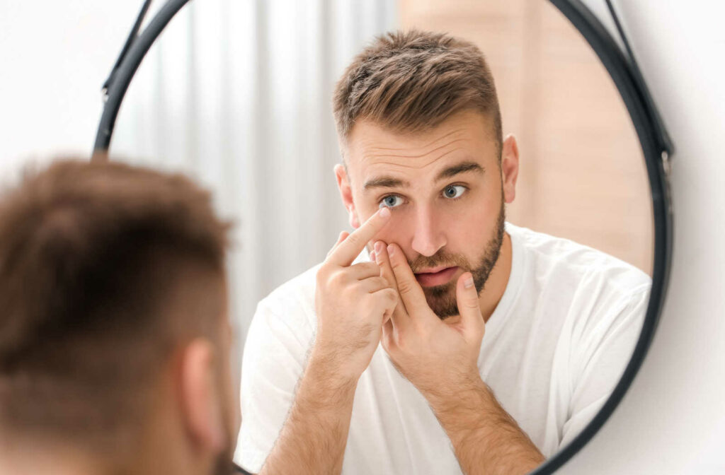 A male looking in the mirror while applying his contact lenses to his eye