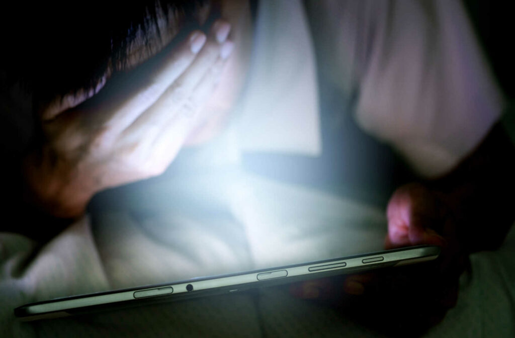A man staring at a tablet screen covering his eyes with his hand
