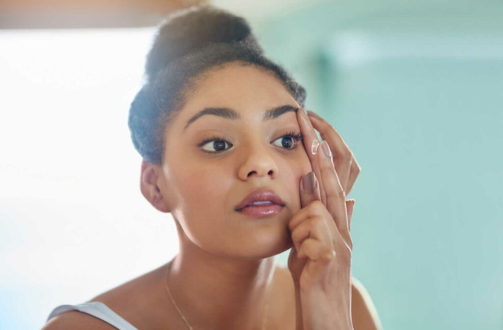 A woman holding her eyelid up with one hand with a contact lens on her finger on the other hand about to put the contact lens in her eye
