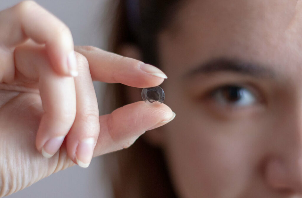 A close-up photo of an orthokeratology lens as a woman holds it between her thumb and index finger close to the camera and in focus.