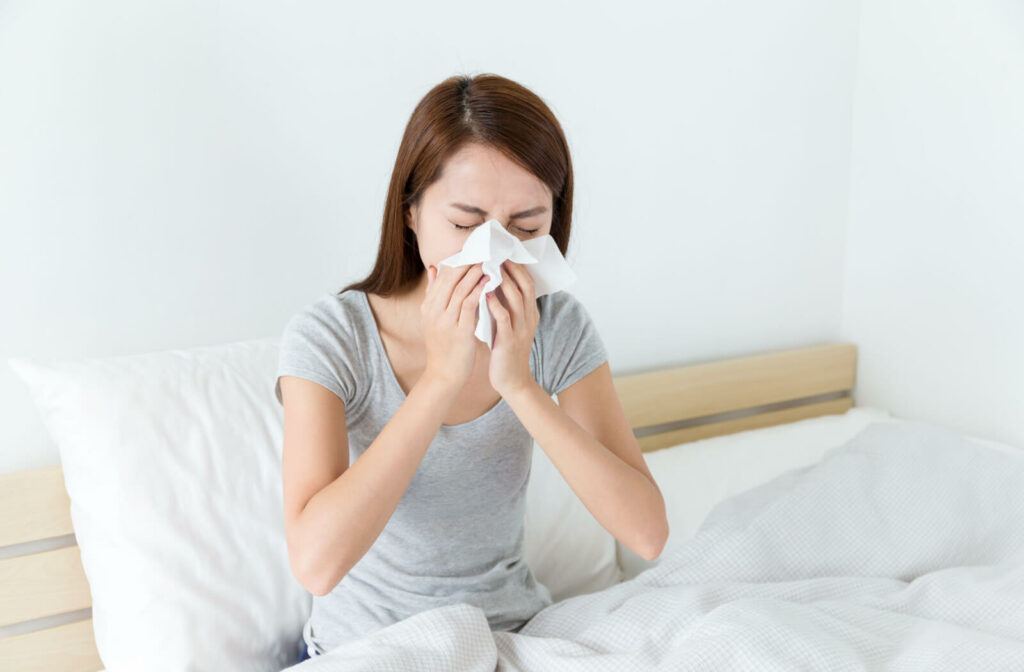 A young woman waking up with dry eyes due to allergies is clearing his nose with tissue paper.