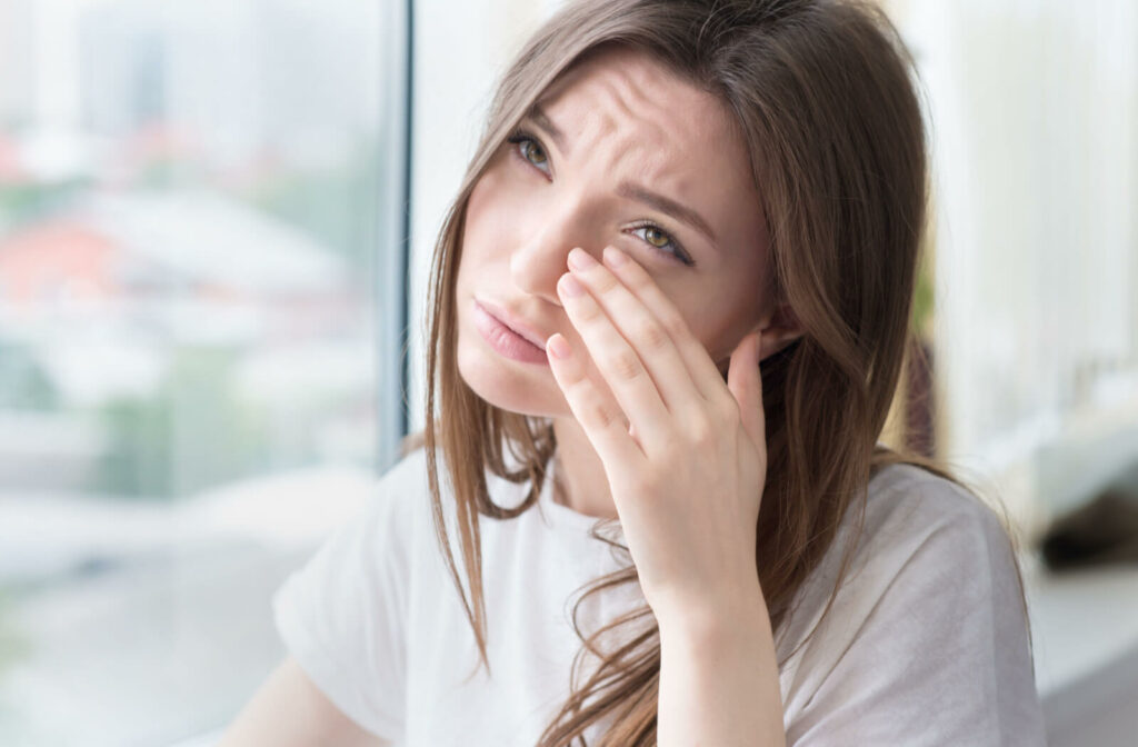 A woman rubbing her left eye lid with her left hand due to eye irritation.