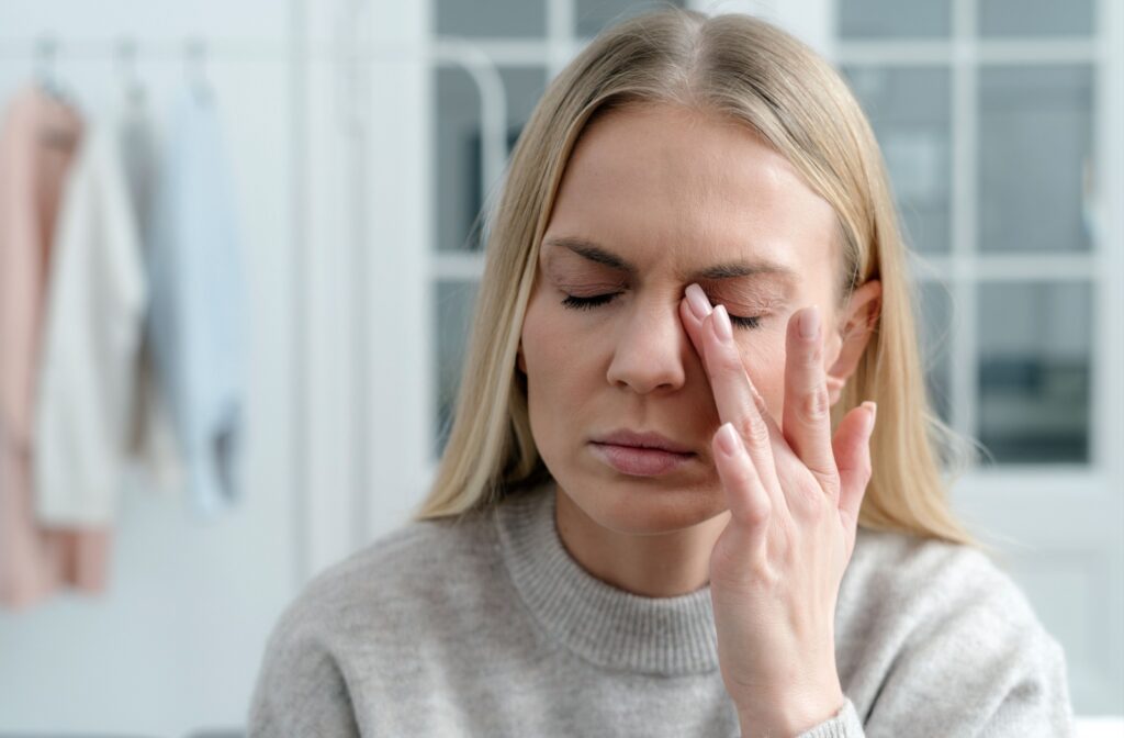 An adult woman has her eyes closed and rubs her left eye with her left hand from discomfort.