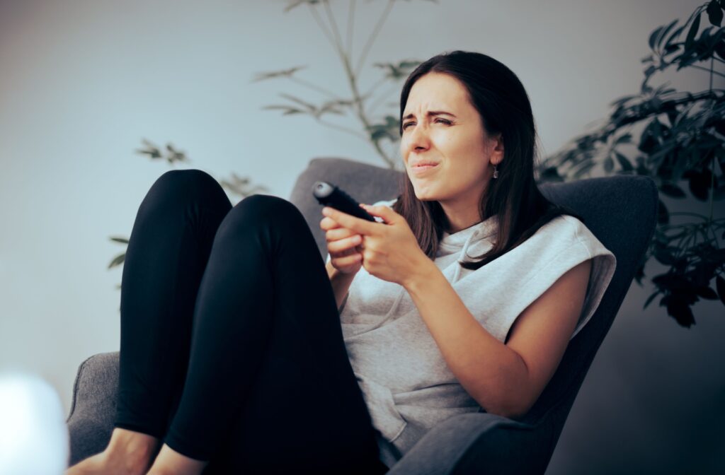 A young adult sitting on a chair and holding a remote, squinting at the TV to try to see clearly.